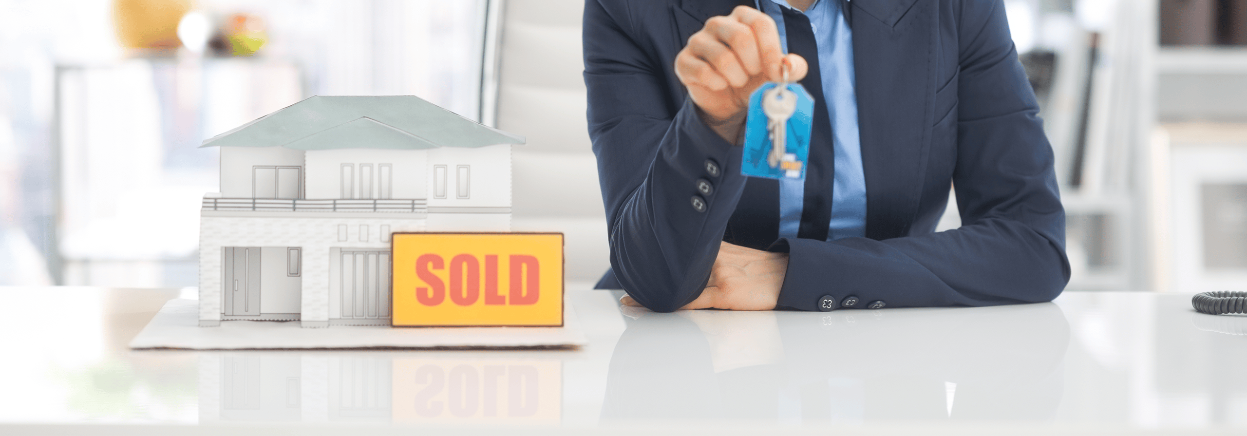 agent holding keys next to a model house with a sold sign next to it